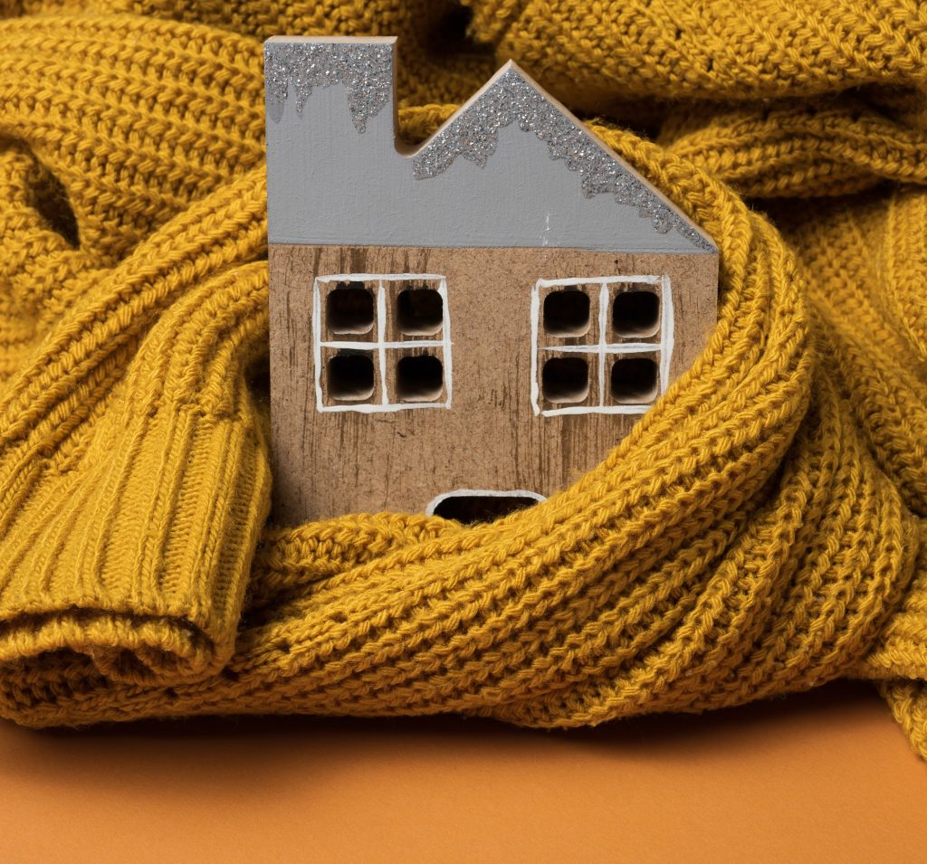 Wooden model of the house is wrapped in a warm knitted sweater. Loan concept for house insulation for domestic page.